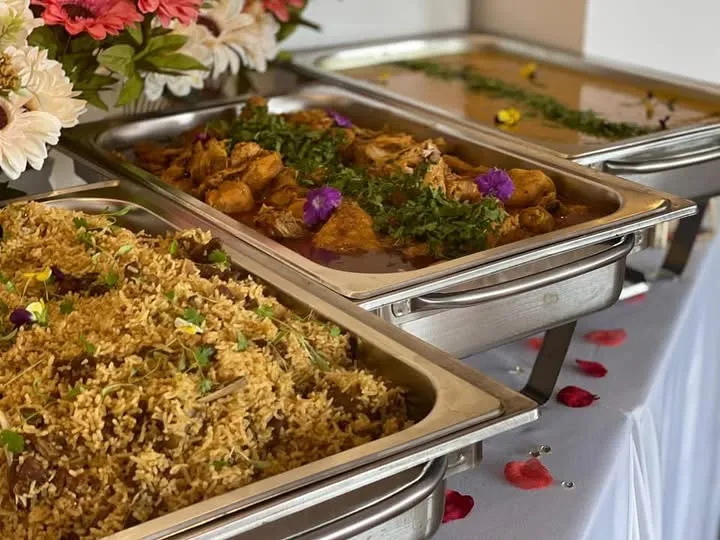 Chafing dishes with biryani and chicken curry, cut flowers and rose petals.