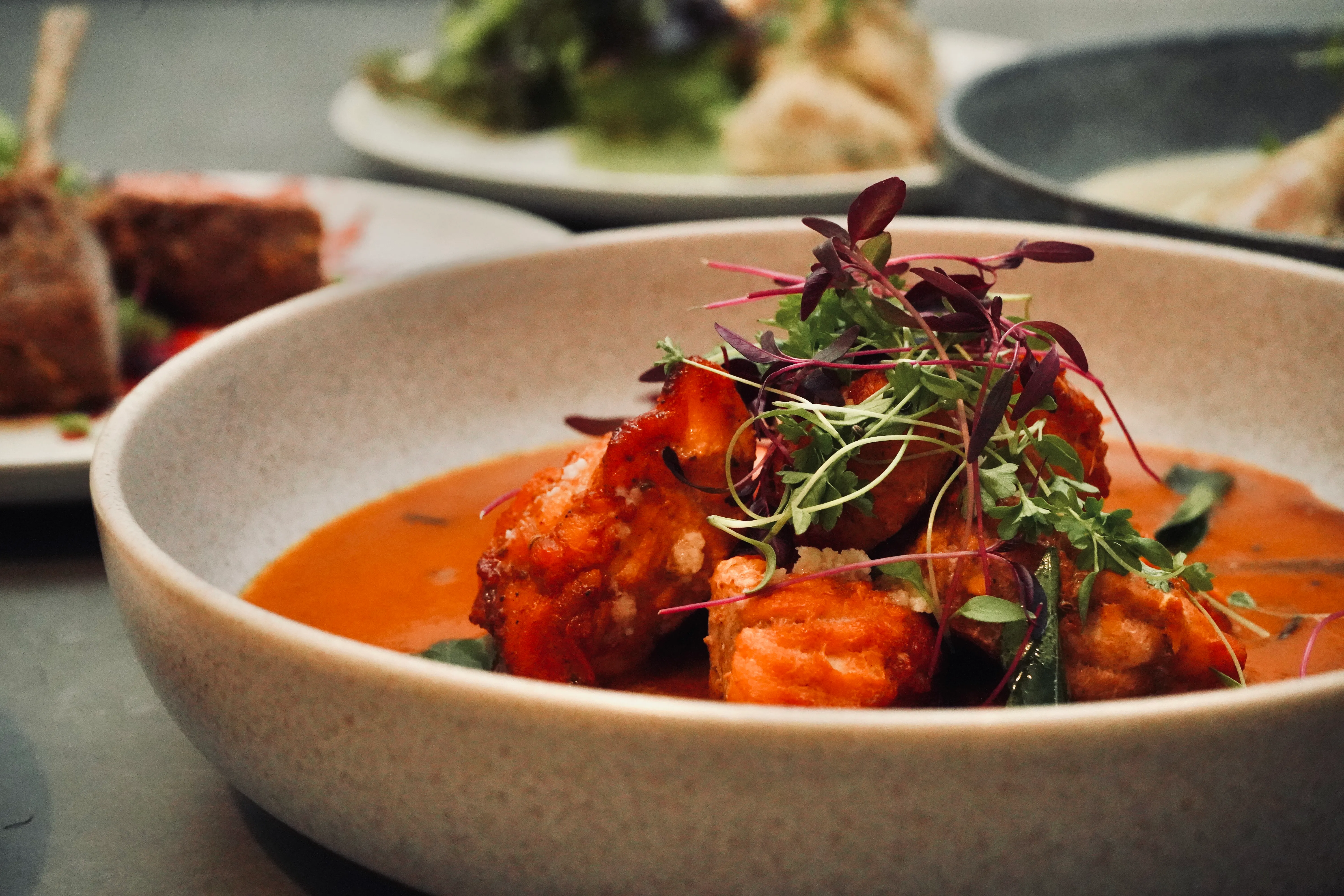 Close-up of a ceramic bowl with orange-red curry, paneer cubes and herb crown.